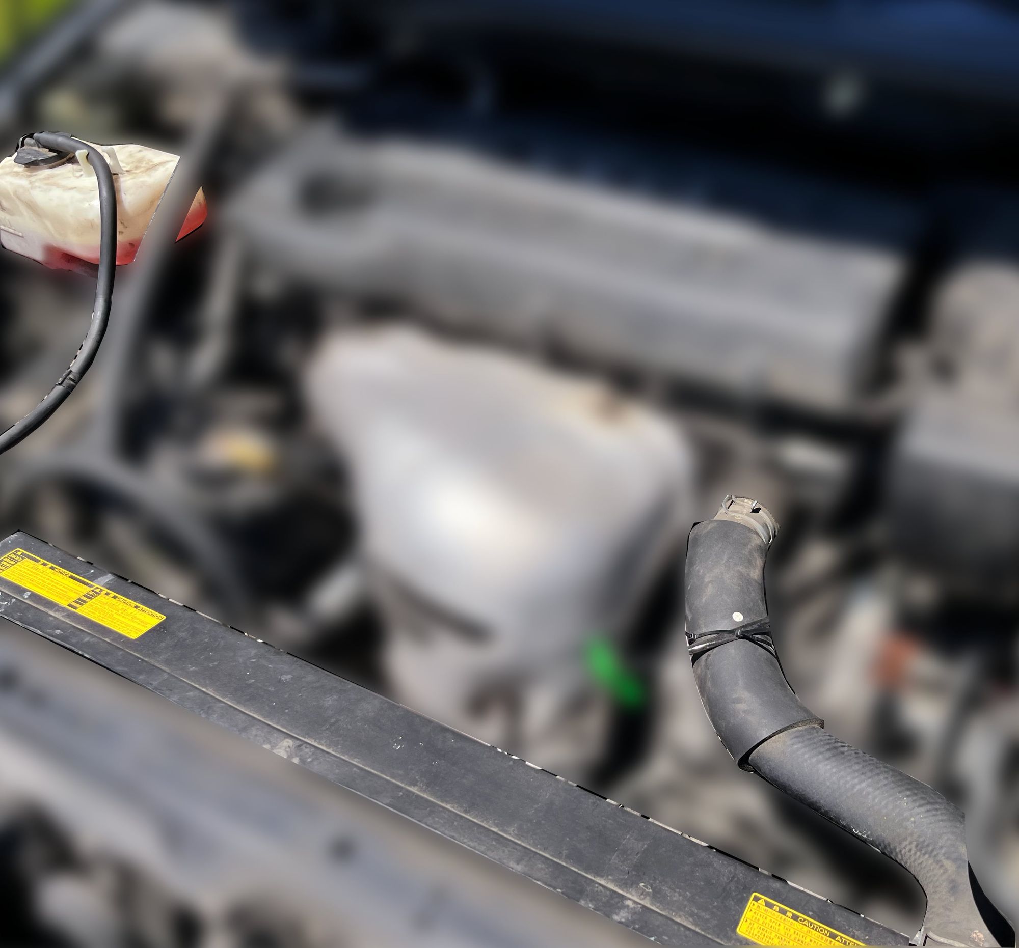 An engine compartment with the coolant system in focus and the rest of the engine and components blurred out.